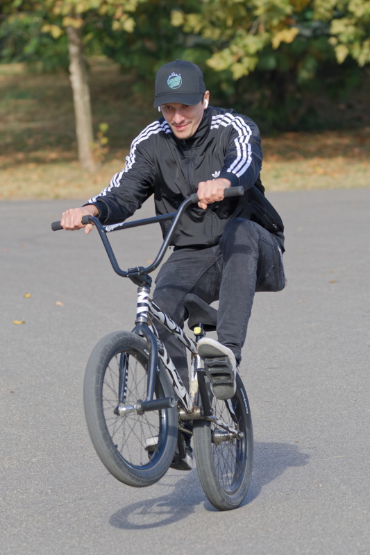 12 - A person performing a BMX manual stunt (balancing on the rear wheel while rolling without pedaling) on a paved surface